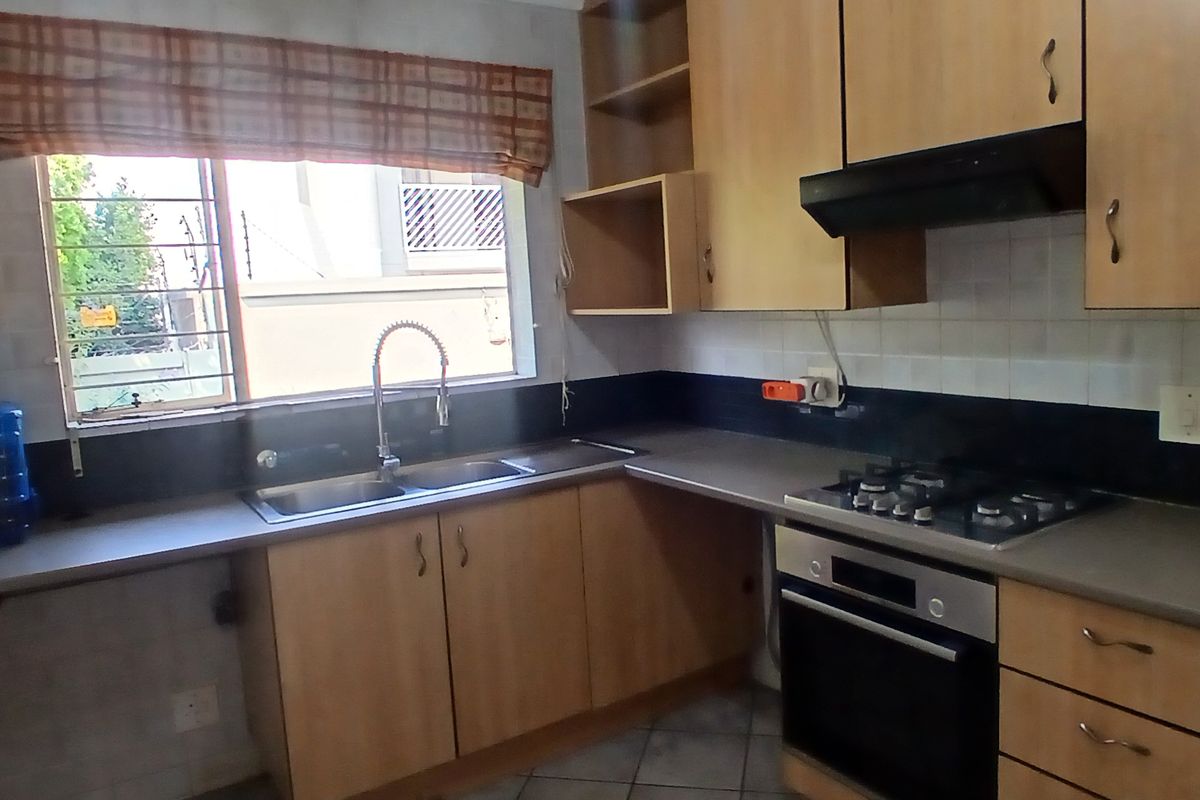 A functional kitchen featuring wooden cabinetry, a gas hob, built-in oven, extractor fan, and a double sink with a window view.