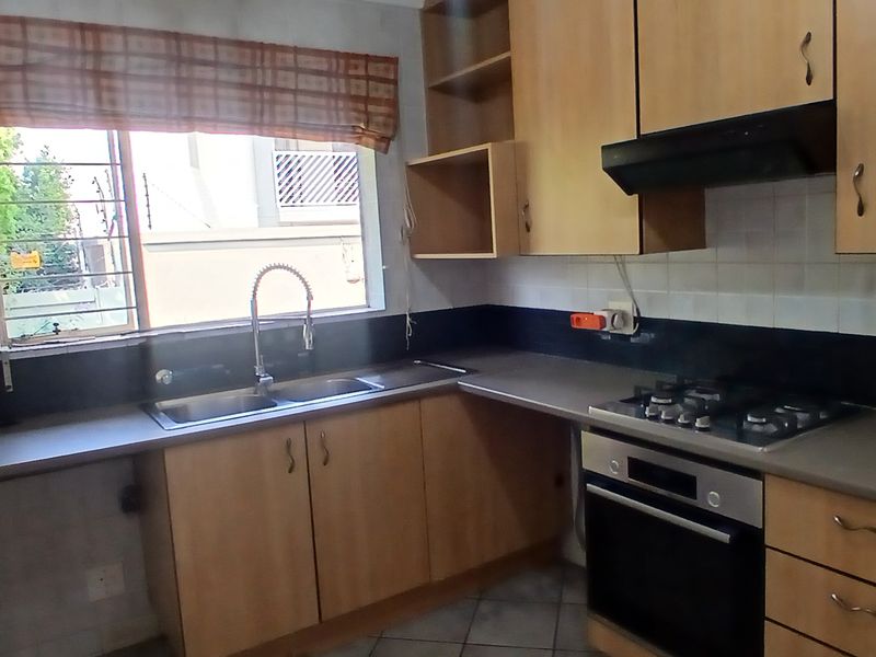 A functional kitchen featuring wooden cabinetry, a gas hob, built-in oven, extractor fan, and a double sink with a window view.