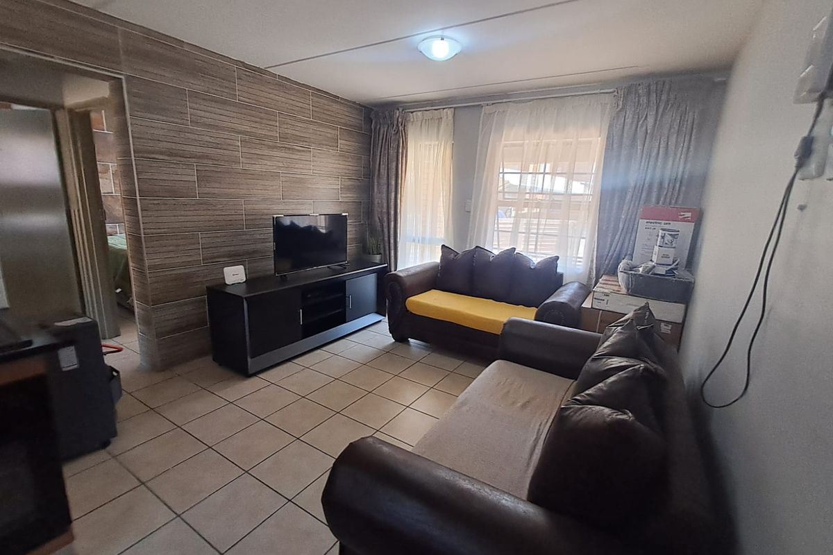 A living room featuring tiled flooring and a textured feature wall, providing a functional space with natural light from the window.