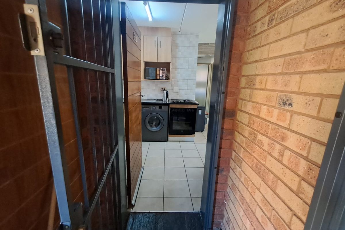 View through a security gate into a functional kitchen featuring tiled floors, built-in cabinetry, and integrated cooking appliances.