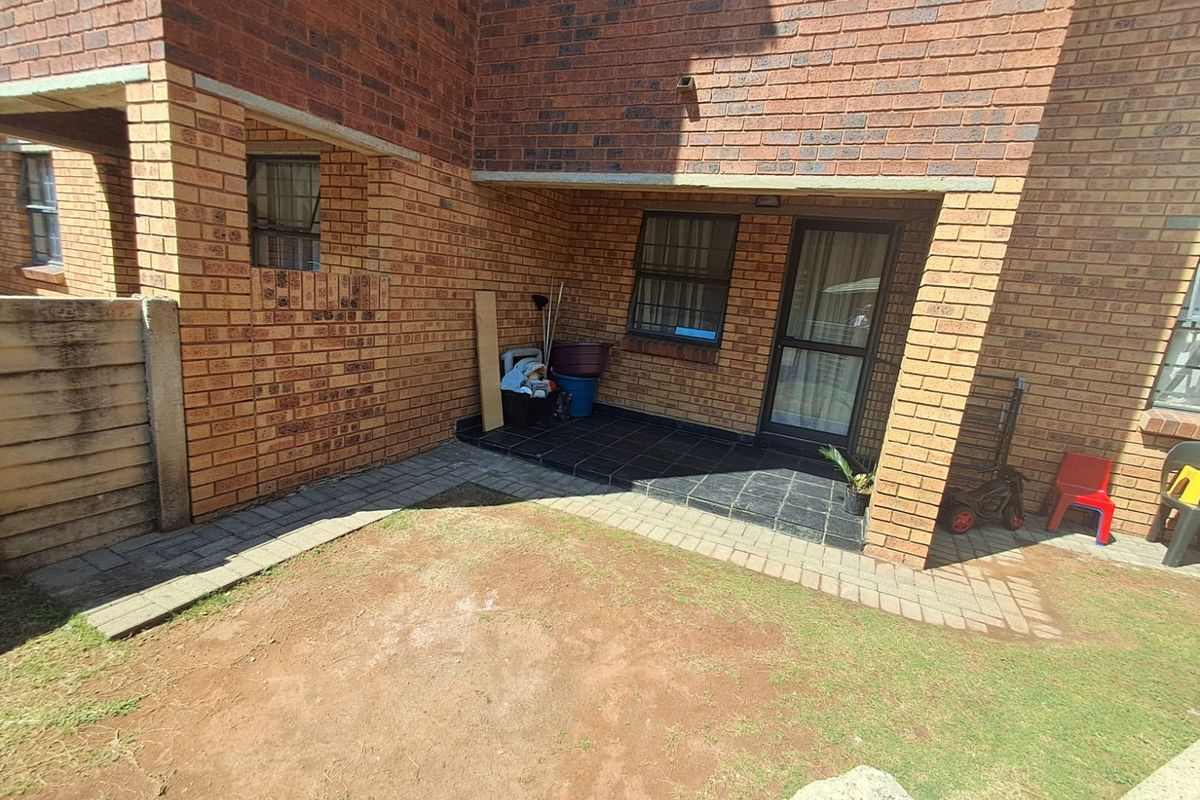 Rear exterior view of a face brick house featuring a small tiled patio area and a paved walkway leading to a garden space.