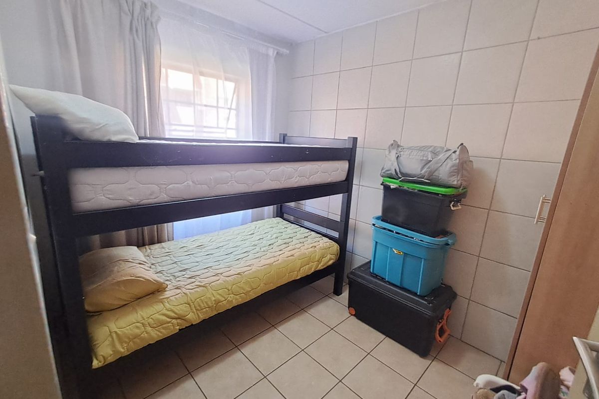 A compact bedroom featuring tiled flooring and tiled wall finishes, equipped with a window and security bars.