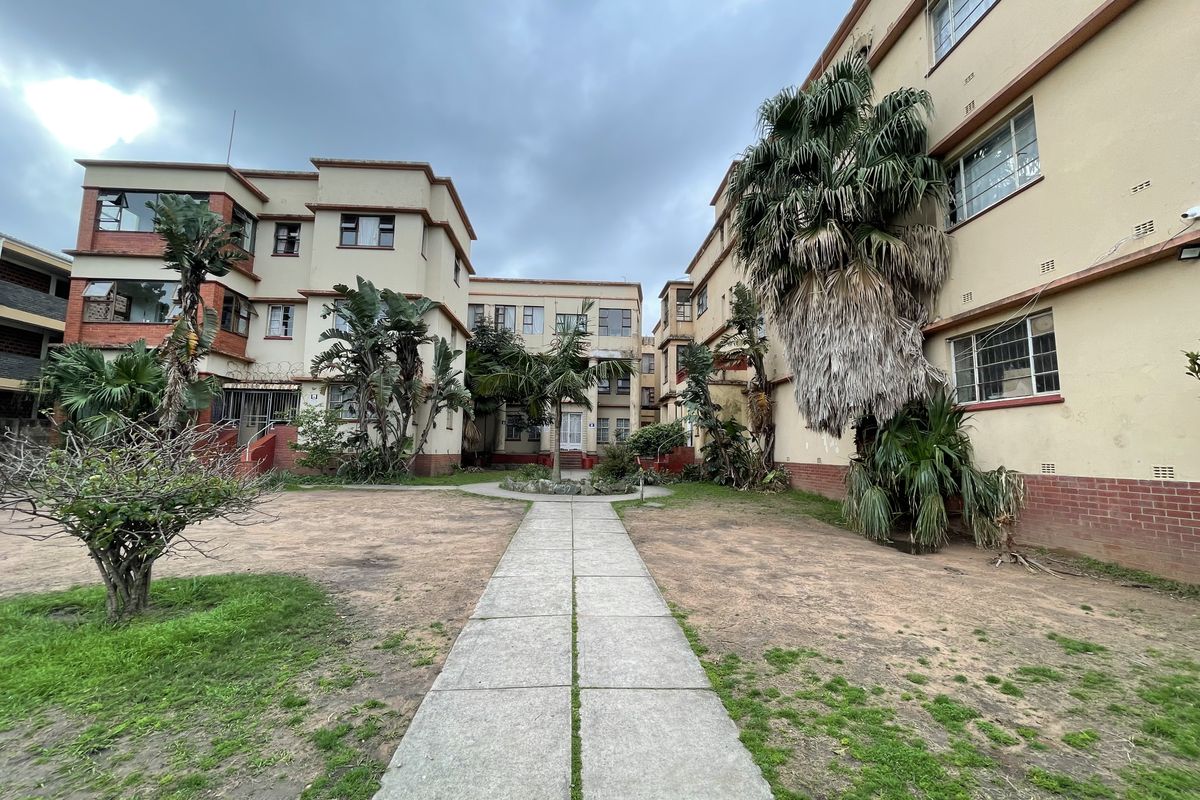 Exterior view of an apartment complex courtyard featuring a central paved walkway, multi-story building facades, and established garden areas.