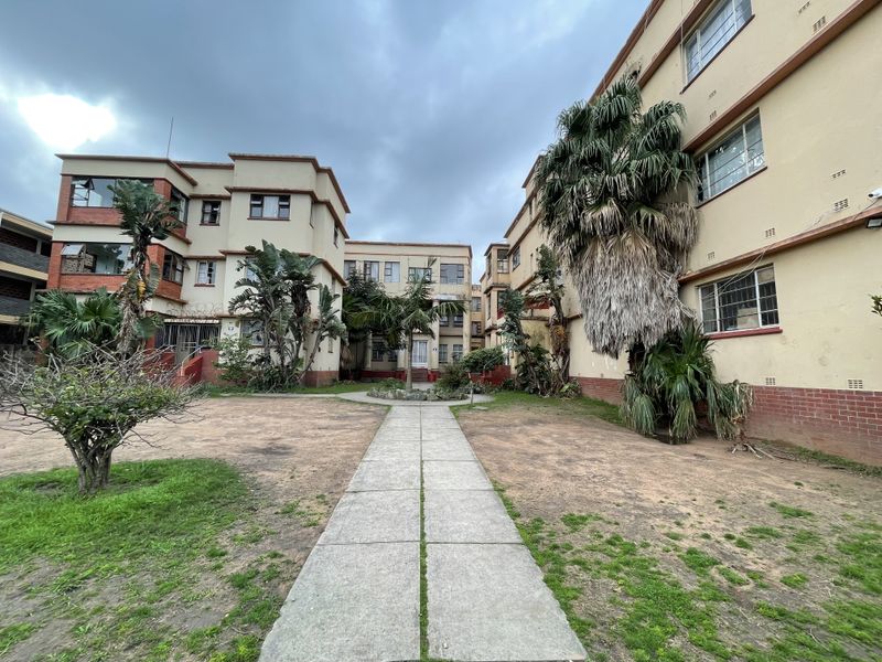 Exterior view of an apartment complex courtyard featuring a central paved walkway, multi-story building facades, and established garden areas.
