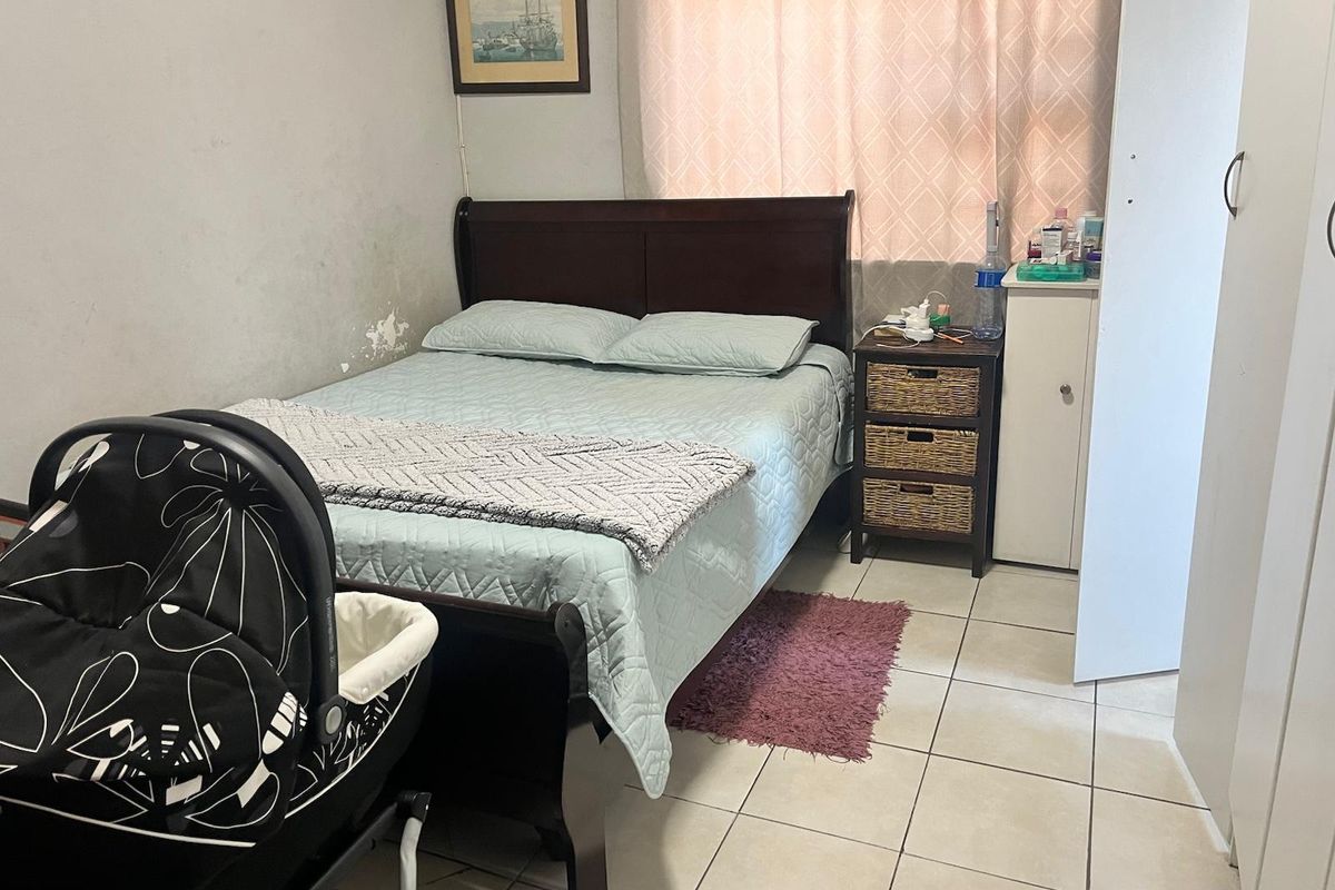 A bedroom featuring tiled flooring and a built-in wardrobe, showing signs of wear including peeling paint on the wall.