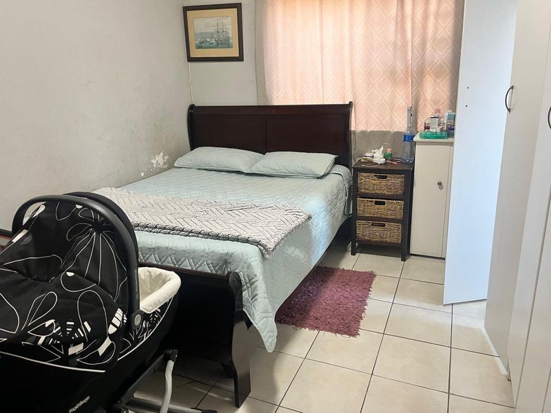 A bedroom featuring tiled flooring and a built-in wardrobe, showing signs of wear including peeling paint on the wall.