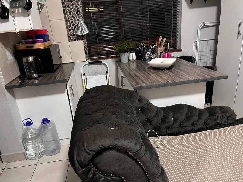 A compact kitchen area featuring laminate countertops, tiled backsplash, and tiled flooring, currently utilized with a mix of functional and personal items.
