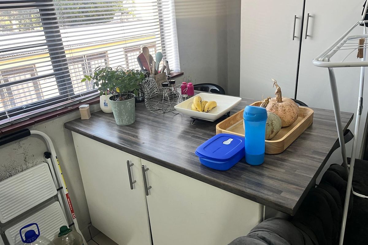 A compact kitchen area featuring a dark laminate countertop and white base cabinetry, complemented by venetian blinds for natural light control.