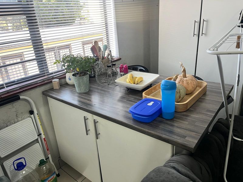 A compact kitchen area featuring a dark laminate countertop and white base cabinetry, complemented by venetian blinds for natural light control.