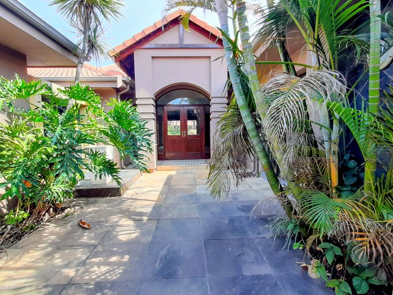 Front entrance featuring a paved walkway leading to a covered arched portico with double timber doors and established garden surrounds.