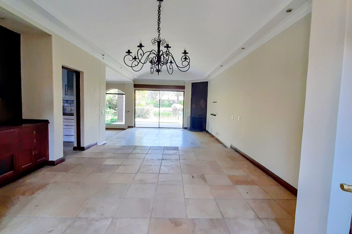Spacious living area featuring stone tile flooring, a decorative wrought iron chandelier, built-in cabinetry, and sliding glass doors leading to the garden.
