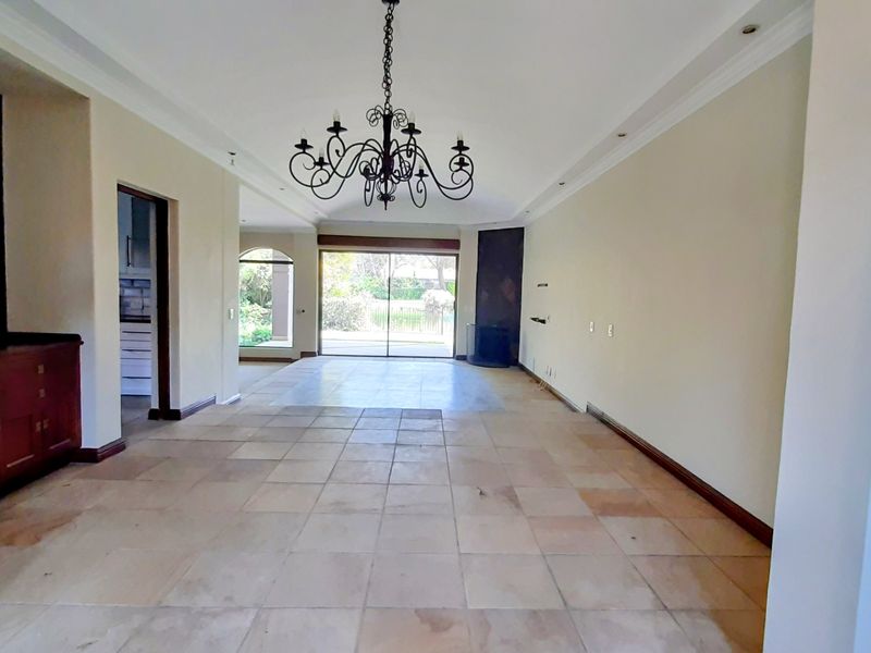 Spacious living area featuring stone tile flooring, a decorative wrought iron chandelier, built-in cabinetry, and sliding glass doors leading to the garden.