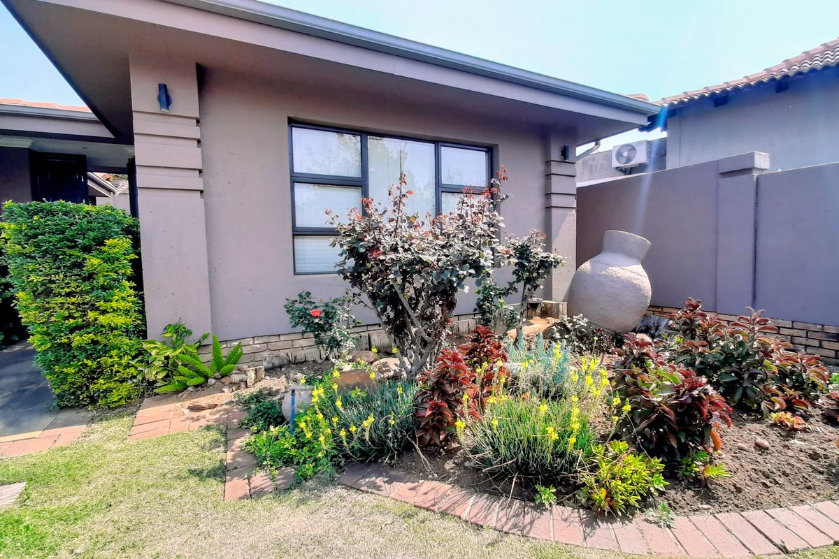 A well-maintained rear garden area featuring landscaped flower beds, brick edging, and modern aluminium window frames on the exterior wall.