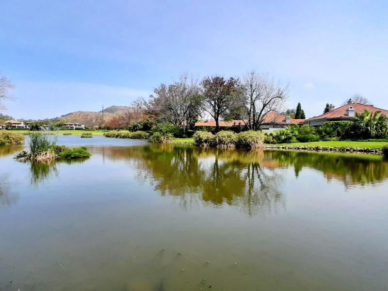 A scenic view of a tranquil lake surrounded by lush landscaped gardens and residential properties in the distance.