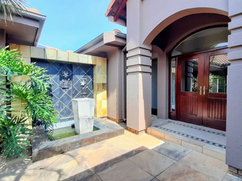 A welcoming entrance featuring a double wooden door, arched architectural detail, and a decorative tiled water feature set within a paved courtyard area.
