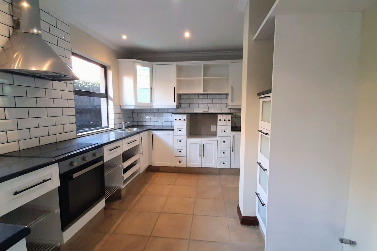 A functional kitchen featuring white cabinetry, subway tile backsplash, built-in oven, and stainless steel extractor fan, with tiled flooring throughout.