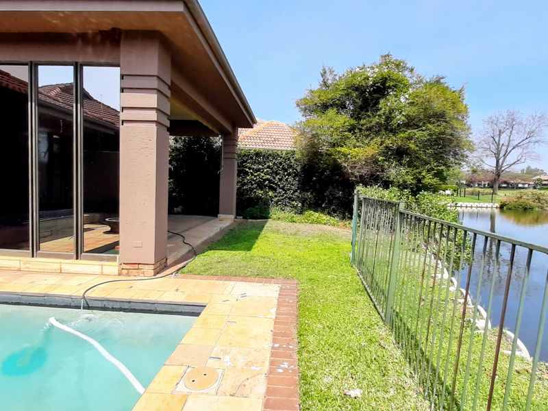 Outdoor pool area featuring a covered patio, stone coping, and metal fencing overlooking a scenic pond.