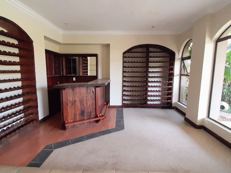 Dedicated bar area featuring custom built-in wooden wine racks, a central bar counter, and large arched windows overlooking the garden.
