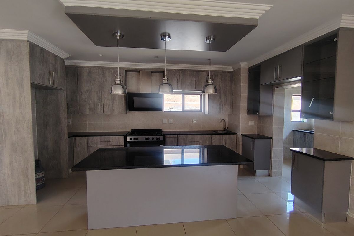 Modern kitchen featuring sleek grey cabinetry, a central island with stone countertops, built-in appliances, and contemporary pendant lighting in an open-plan layout.