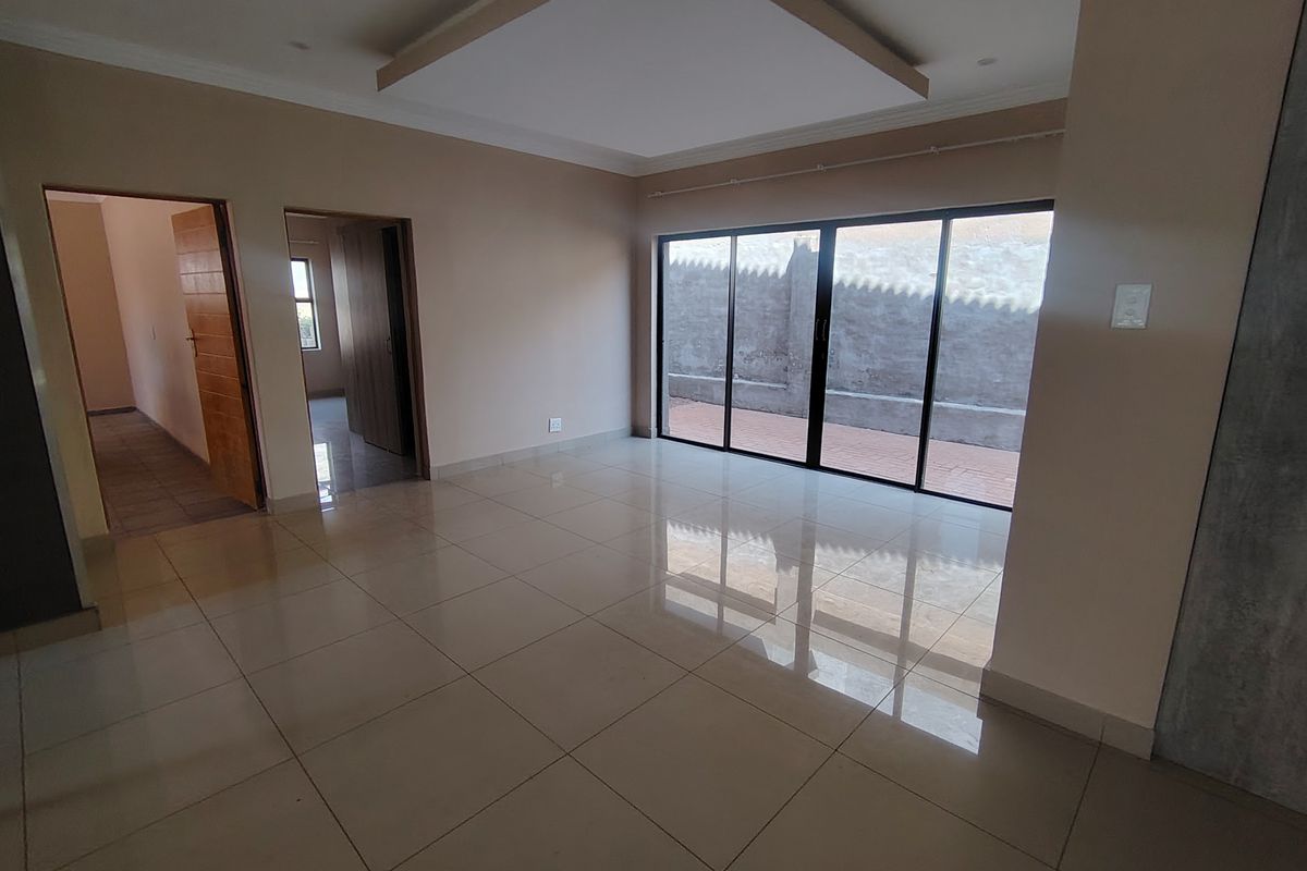 A spacious, empty living area featuring polished tile flooring, a modern recessed ceiling design, and large sliding glass doors leading to an outdoor patio.
