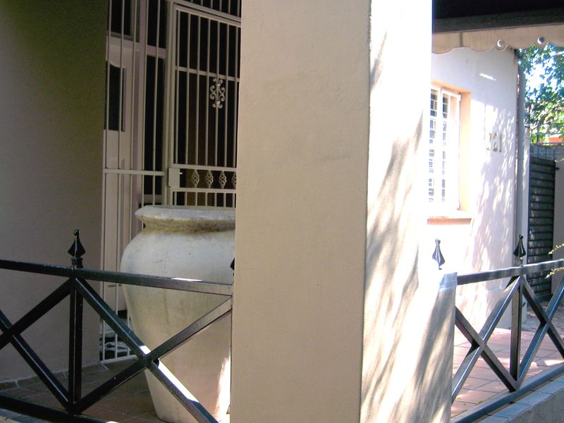 A covered patio area featuring tiled flooring, a concrete support pillar, and a metal security gate at the entrance.