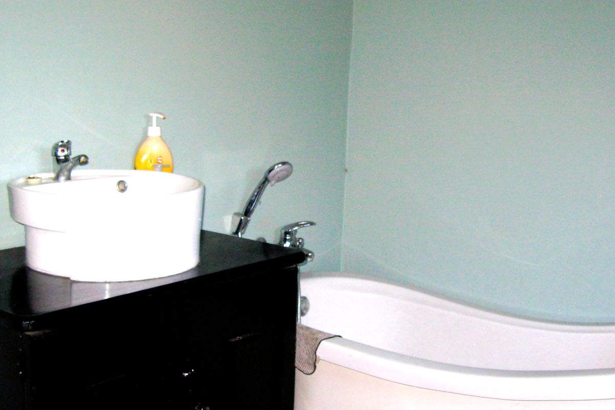 A bathroom featuring a black vanity cabinet with a white vessel sink and a freestanding bathtub with a handheld shower mixer.