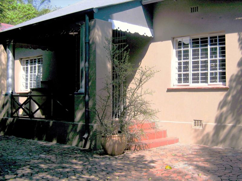 Front facade of the house featuring a covered patio, security bars on windows, tiled entrance steps, and a cobblestone driveway.