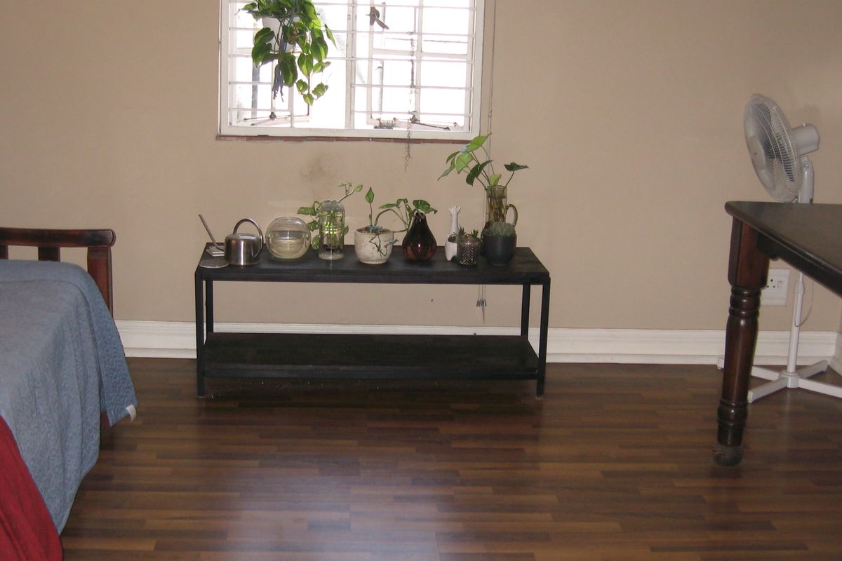 A bedroom featuring dark laminate flooring, neutral wall paint, and a window fitted with security bars.