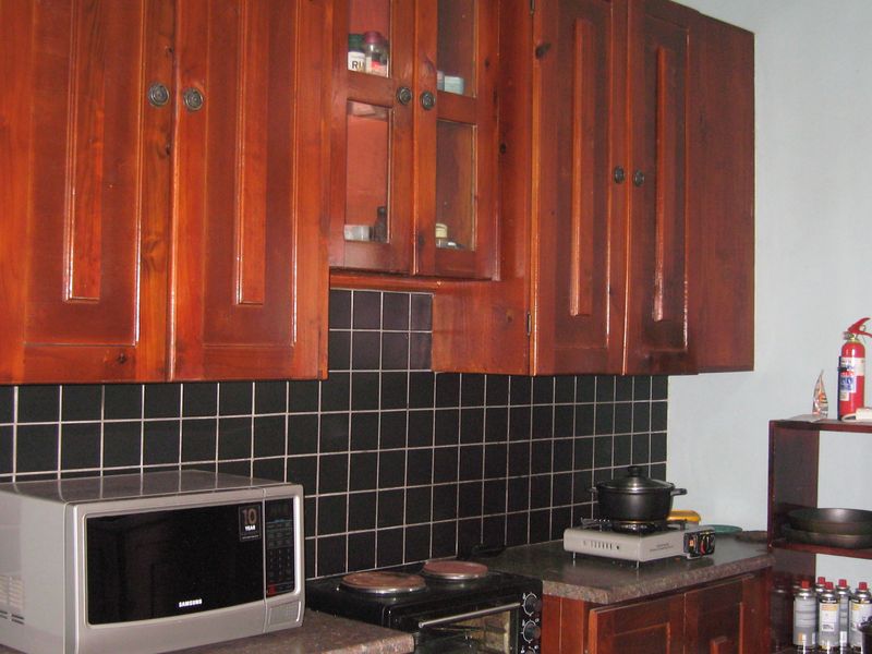 A kitchen area featuring dark wooden cabinetry, a black tiled backsplash, and a laminate countertop with a built-in oven.
