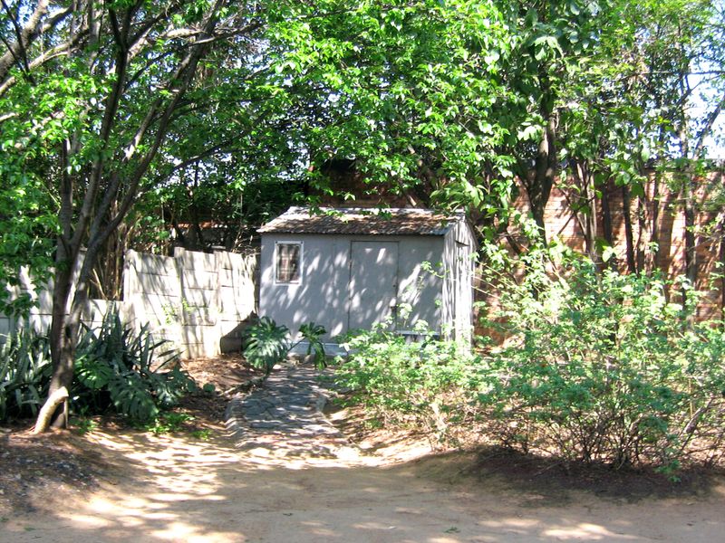 A secluded garden area featuring a storage shed, stone pathway, and mature trees enclosed by a precast concrete boundary wall.