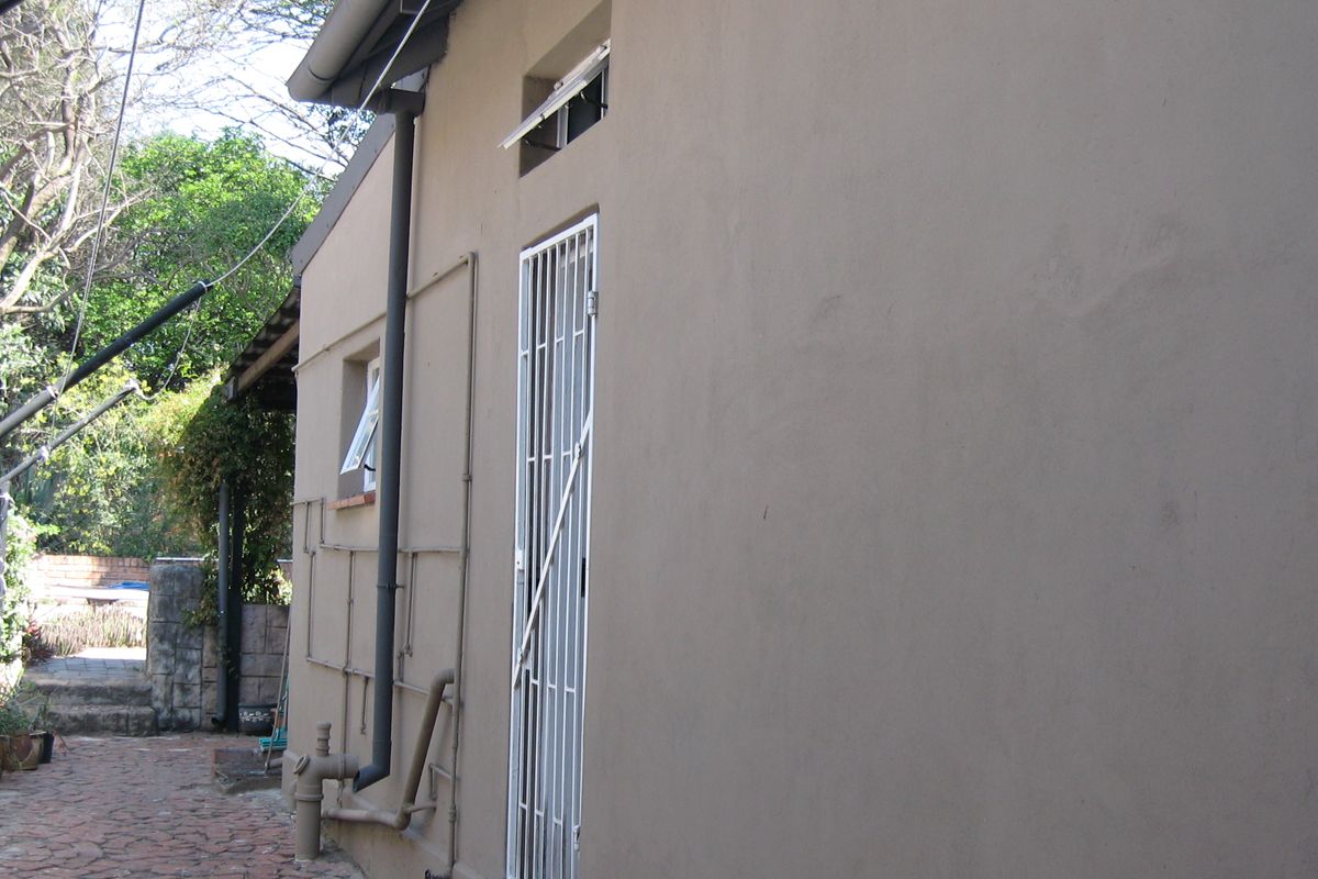 A view of the rear exterior wall featuring a security gate, downpipe, and paved walkway along the side of the house.