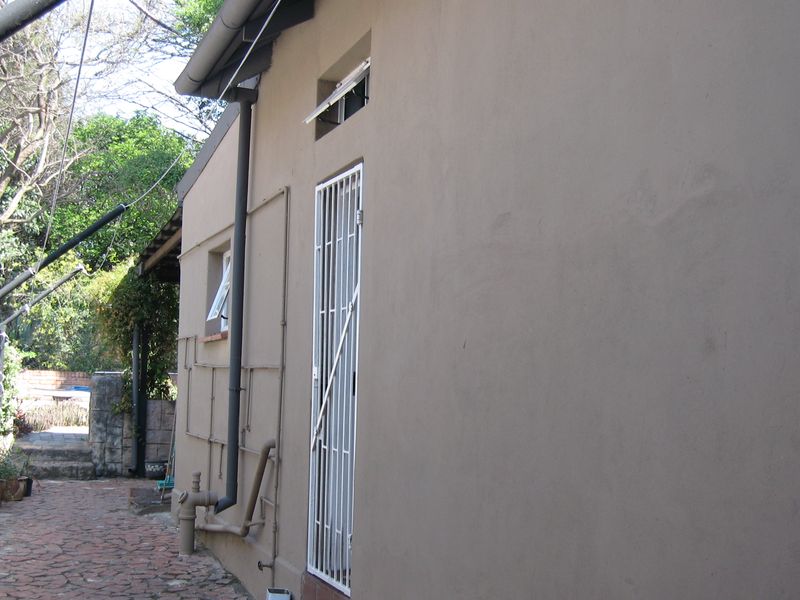 A view of the rear exterior wall featuring a security gate, downpipe, and paved walkway along the side of the house.
