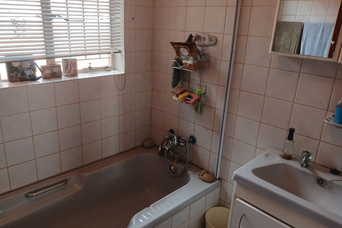 A dated bathroom featuring a standard bathtub, vanity basin, and wall tiling, requiring modernization to improve its overall condition and aesthetic appeal.