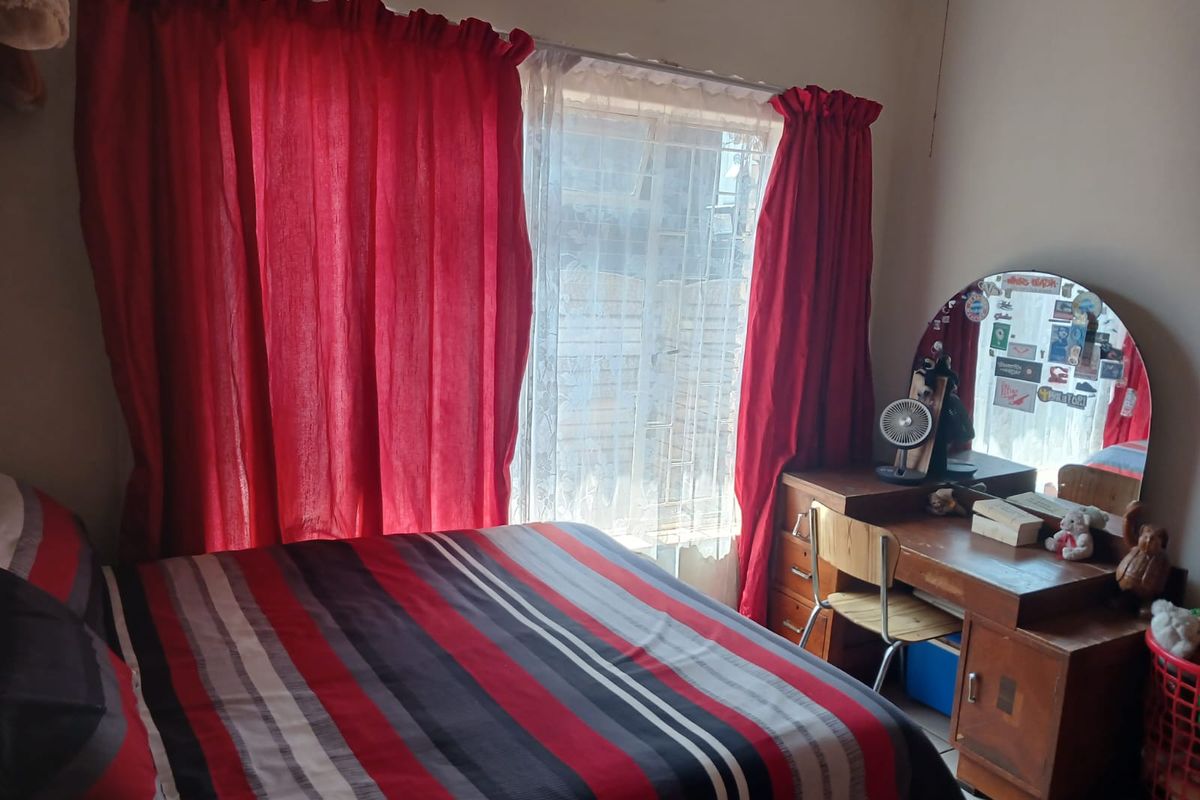 A functional bedroom featuring a wall-mounted split-system air conditioner and window security bars.