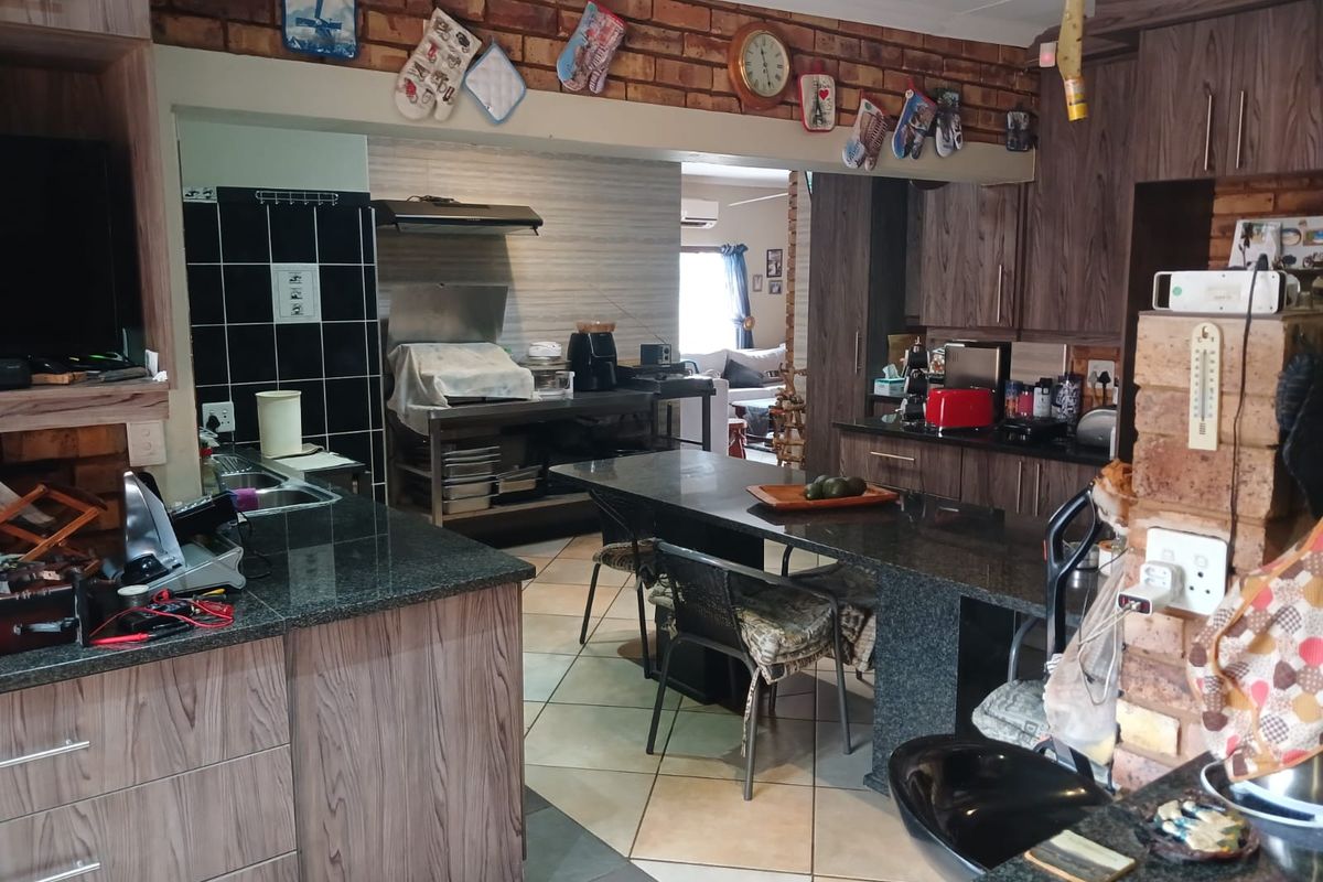 A functional kitchen featuring granite countertops, ample built-in cabinetry, an extractor fan, and a breakfast bar, finished with a rustic exposed brick wall.