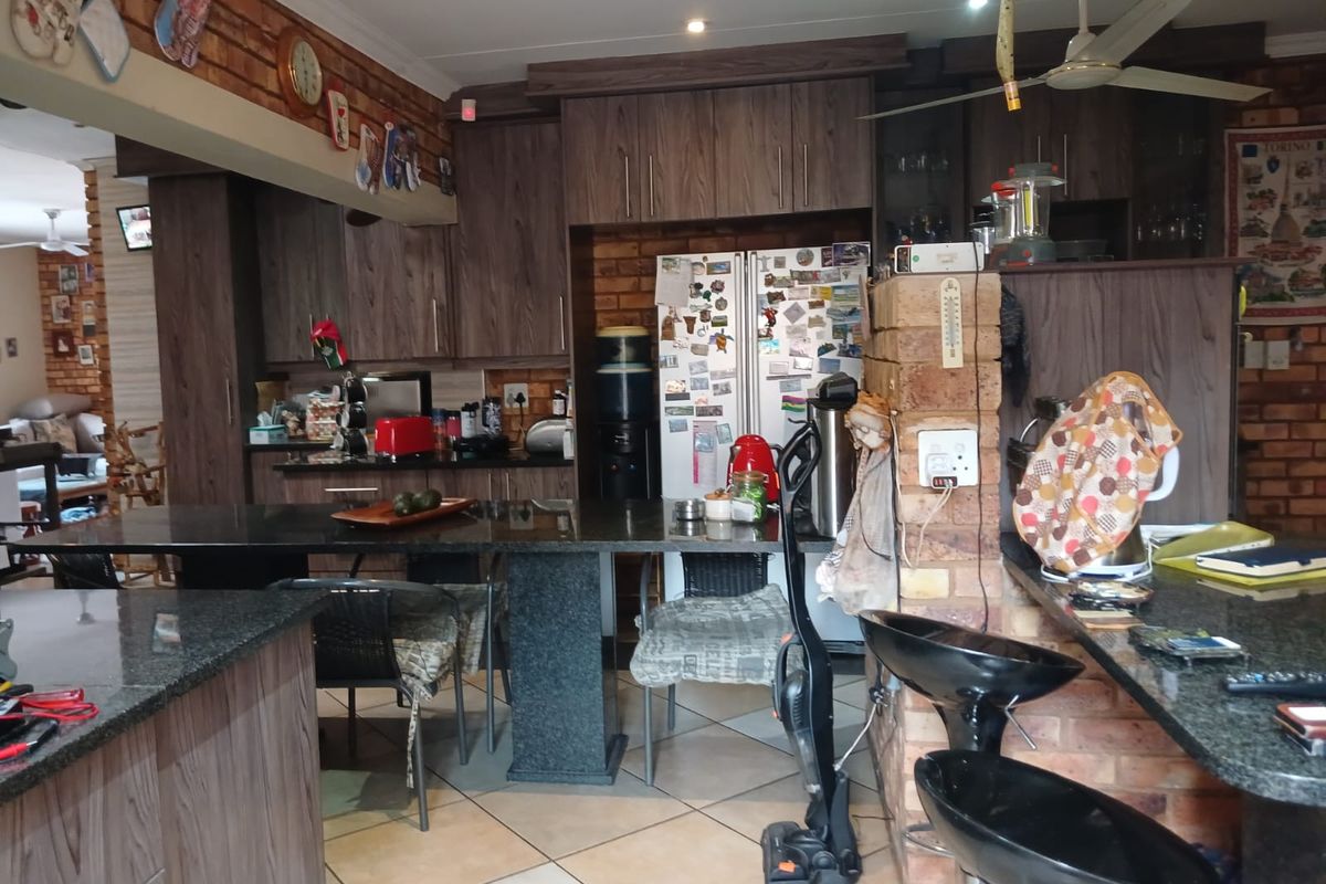 A kitchen featuring dark wood cabinetry, granite countertops, and exposed brick accents, with an open-plan layout connecting to the living area.