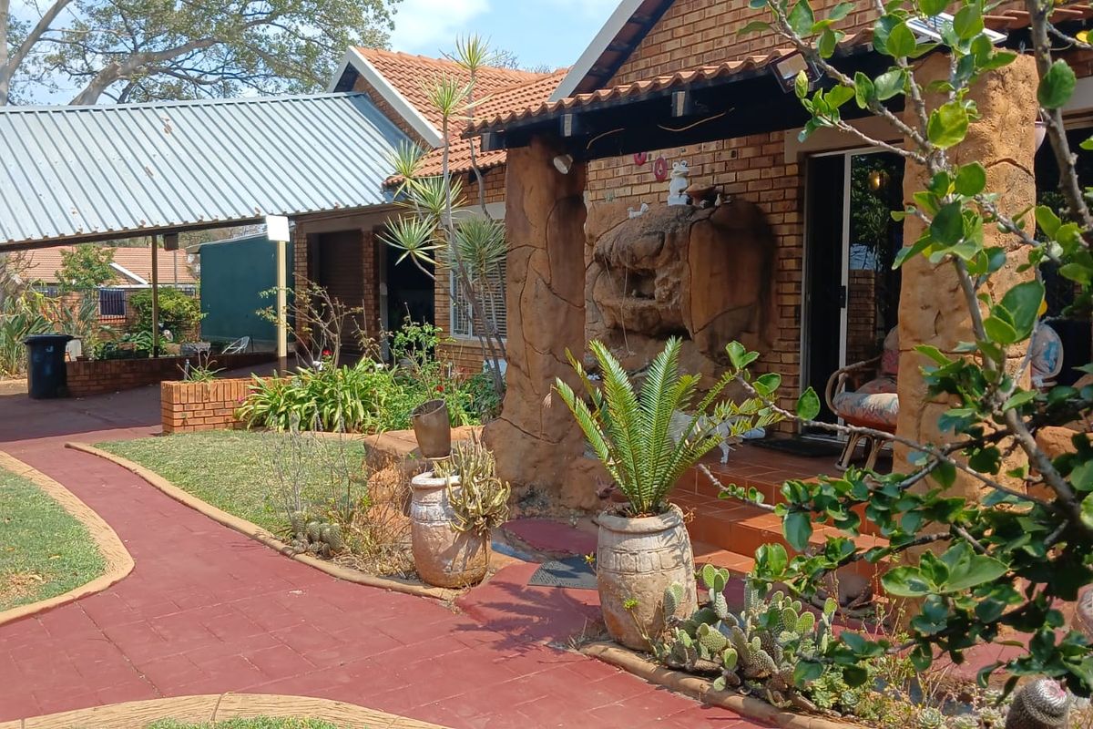 Rear exterior view featuring a brick facade, covered patio with decorative stone pillars, and a paved walkway leading to a carport area.
