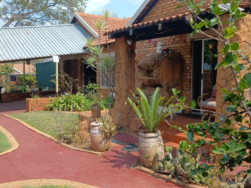 Rear exterior view featuring a brick facade, covered patio with decorative stone pillars, and a paved walkway leading to a carport area.