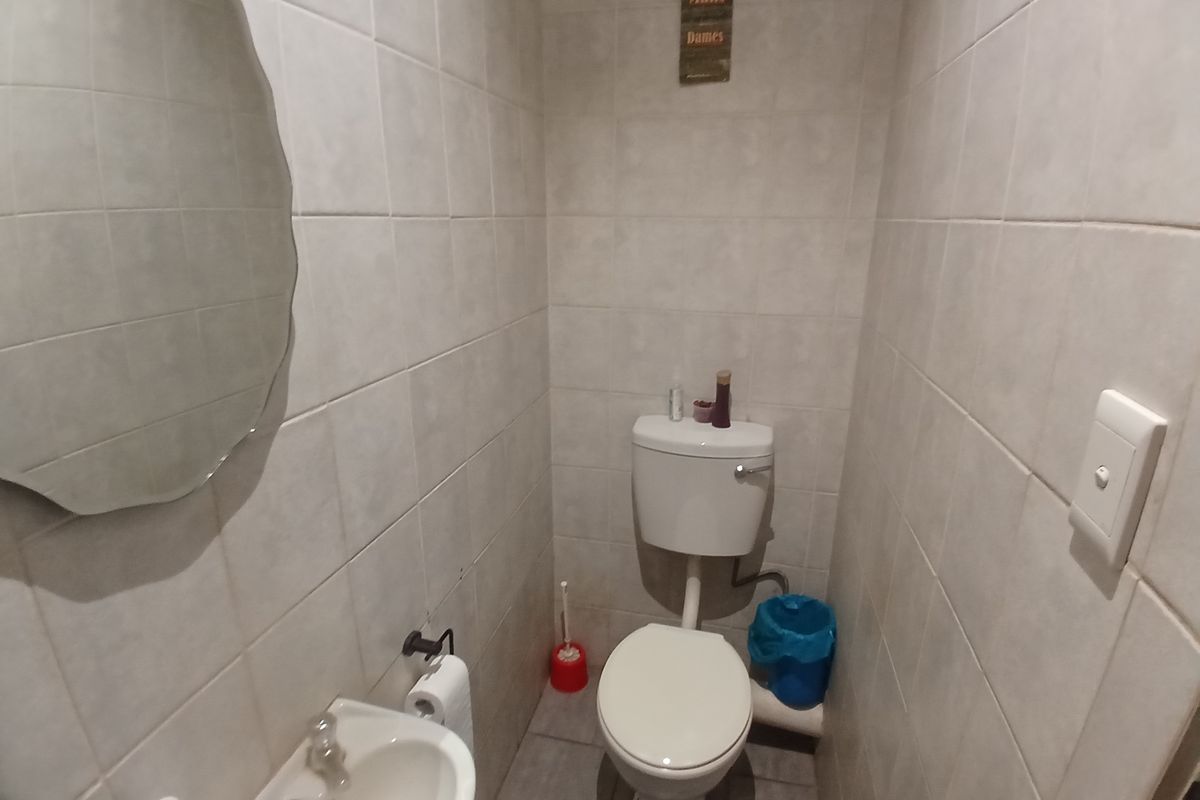A compact guest bathroom featuring a toilet, wall-mounted basin, and neutral floor-to-ceiling wall tiling.