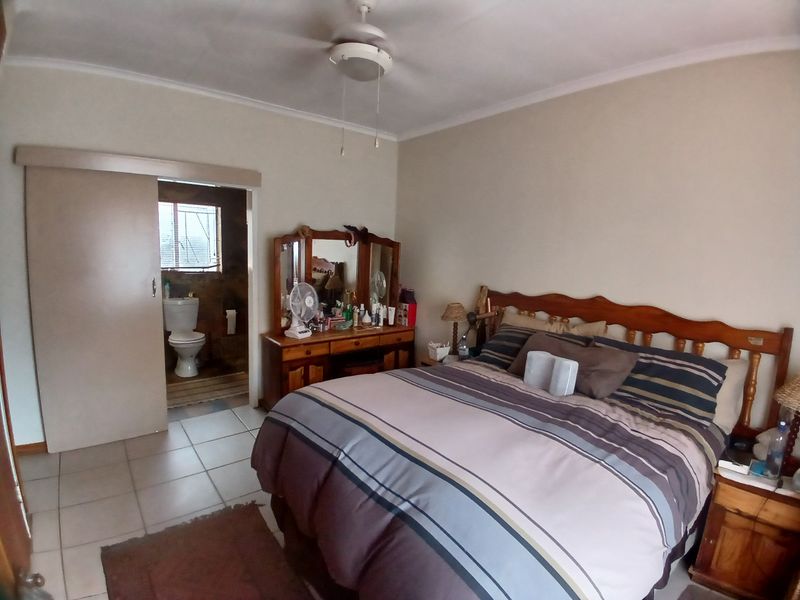A bedroom featuring tiled flooring, a ceiling fan, and an adjoining en-suite bathroom accessed via a sliding door.