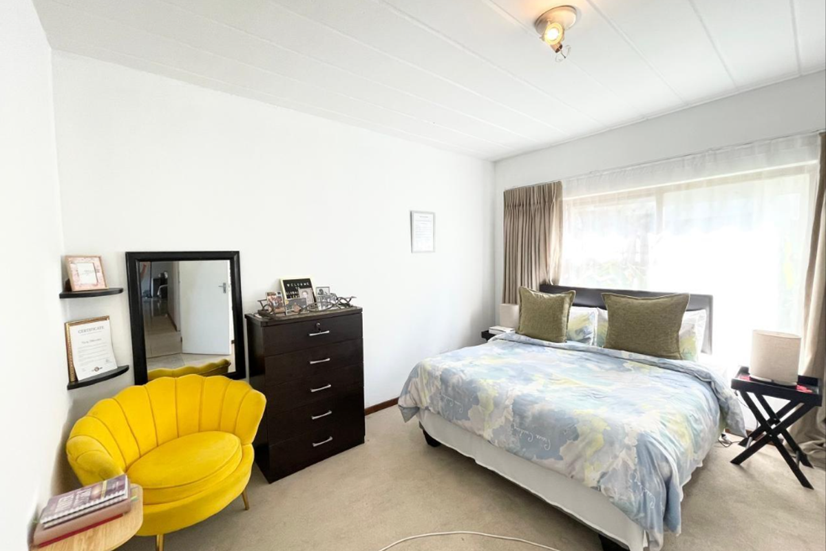 A well-lit bedroom featuring carpeted flooring, built-in corner shelving, and a large sliding window with curtain tracks.