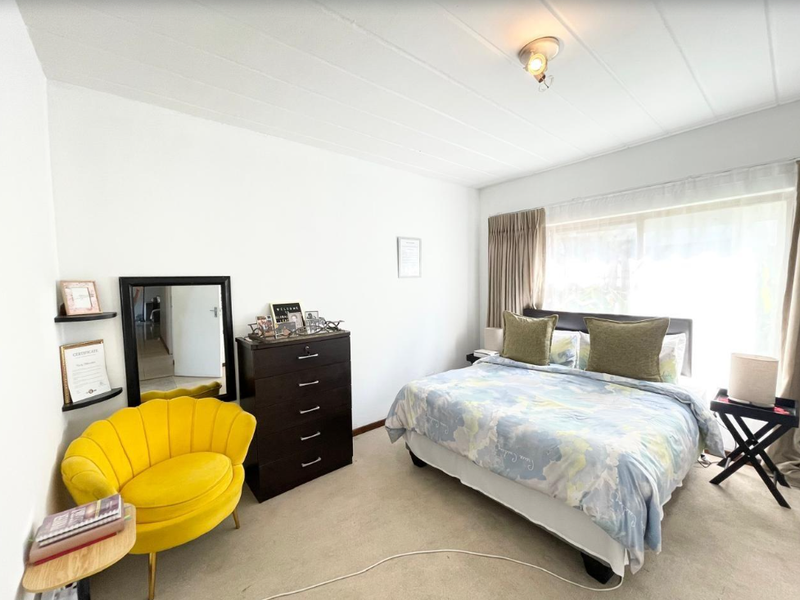 A well-lit bedroom featuring carpeted flooring, built-in corner shelving, and a large sliding window with curtain tracks.