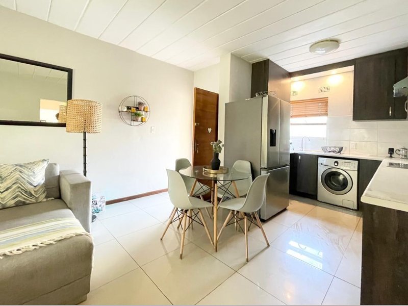 Open-plan living and kitchen area featuring modern dark cabinetry, tiled flooring, and integrated laundry facilities in a well-maintained apartment setting.