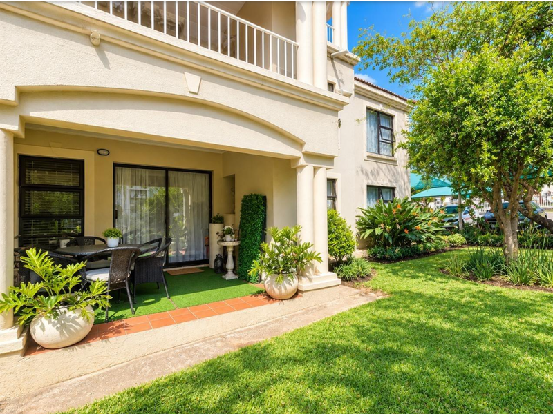 A covered ground-floor patio featuring tiled flooring and sliding glass doors, overlooking a well-maintained private garden area.