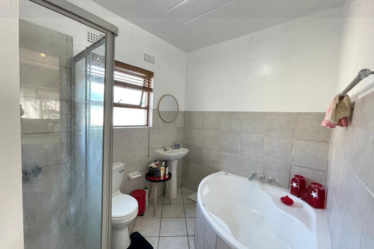 A functional bathroom featuring a corner bathtub, separate shower enclosure, and pedestal basin with neutral wall and floor tiling.