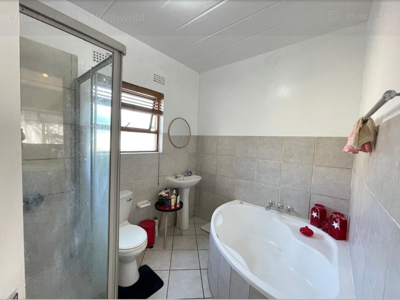 A functional bathroom featuring a corner bathtub, separate shower enclosure, and pedestal basin with neutral wall and floor tiling.