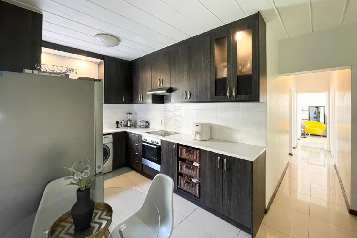 A functional kitchen featuring dark wood cabinetry, white countertops, tiled backsplash, and integrated appliances, with direct access to the hallway.
