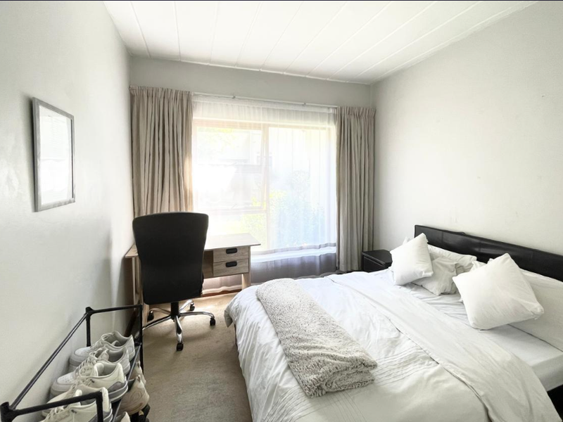 A functional bedroom featuring neutral carpet flooring, a panelled ceiling, and a large window with curtain tracks, providing natural light to the space.