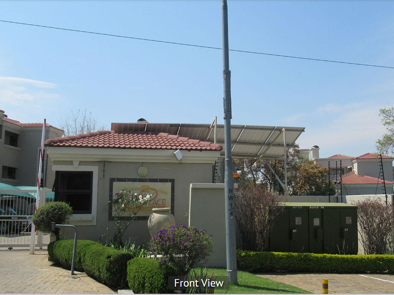 Front entrance view of the apartment complex featuring a security guard house, gated access, and solar panel installation.