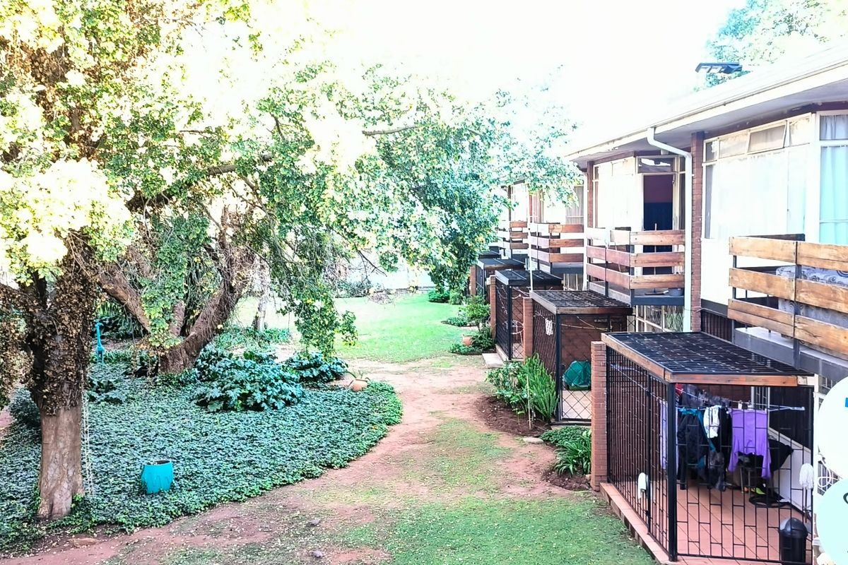 Rear view of the townhouse complex featuring wooden balconies, brick exterior walls, and a shared garden area with mature trees.